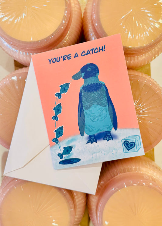 Greeting card with a penguin illustration and 'You're a Catch!' text, surrounded by wrapped products.