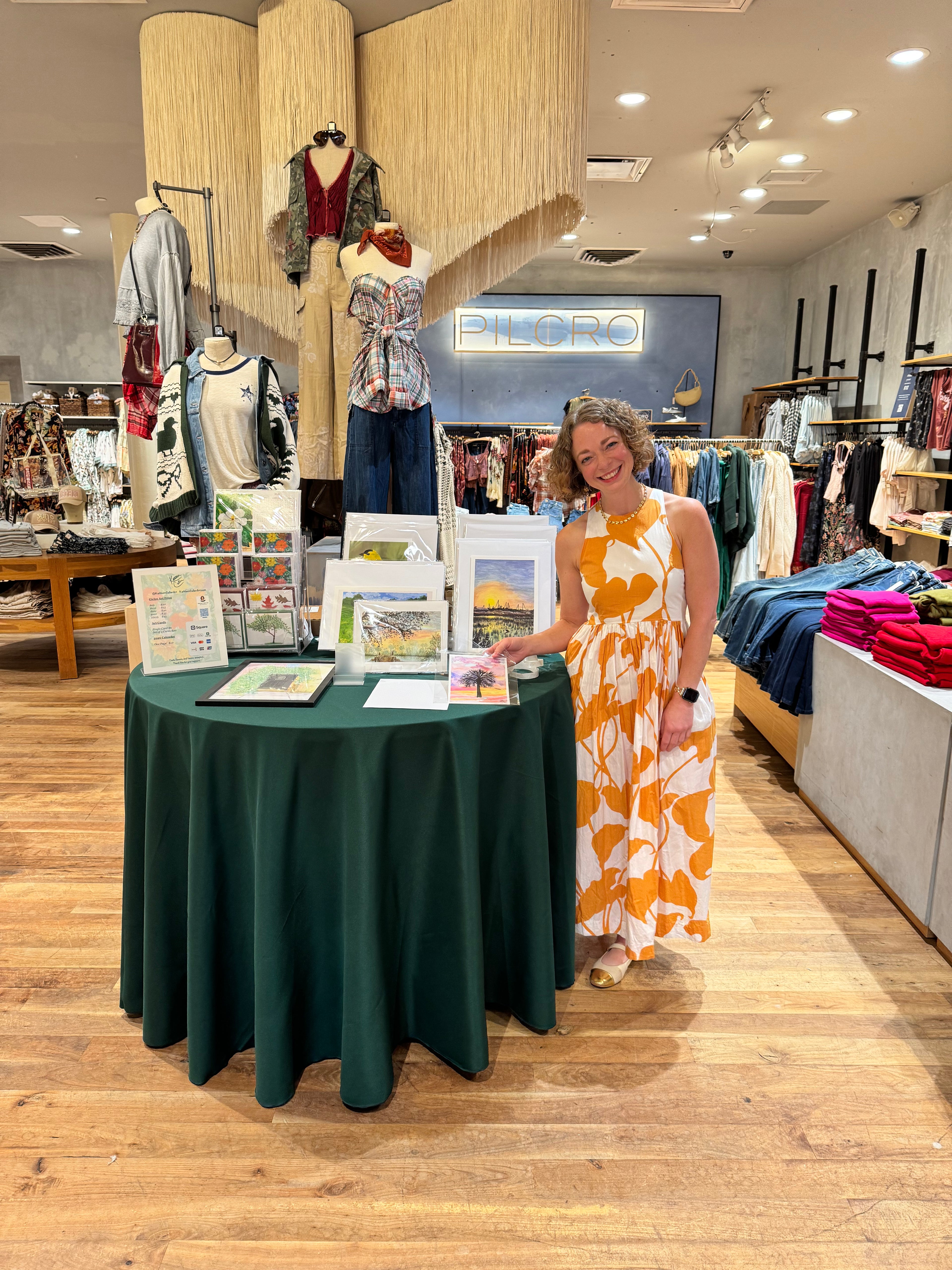 Artist Kathleen Culler standing next to a table with brochures in a clothing store